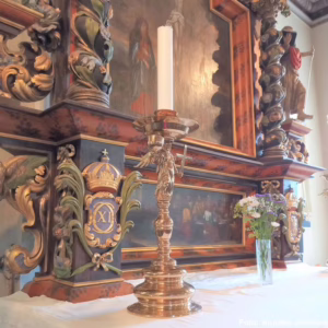 En ljusstake i mässing som ser ut som en ängel med vingar som står i Kungälvs kyrka.